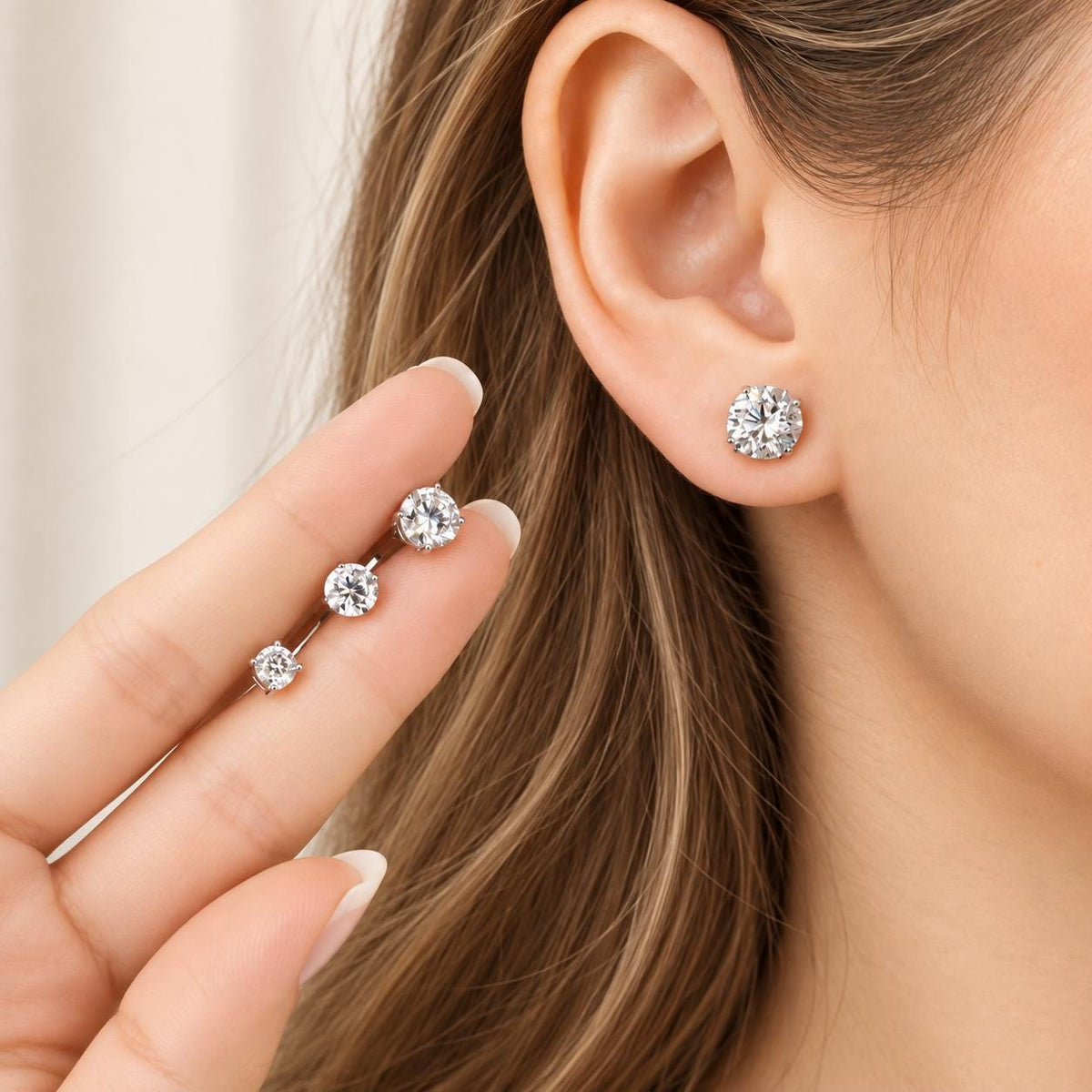 Hand holding moissanite studs showing size difference